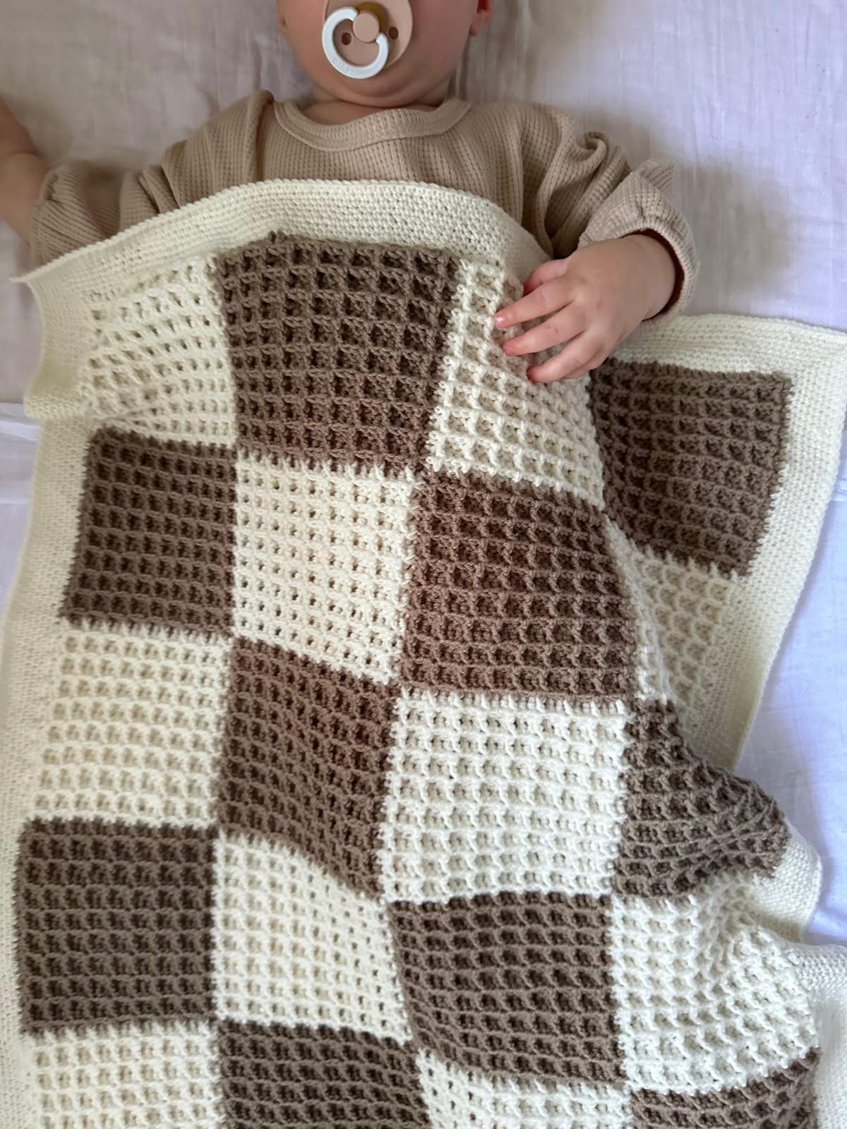 Handmade cream and taupe crochet baby blanket with a patchwork texture, shown with a baby