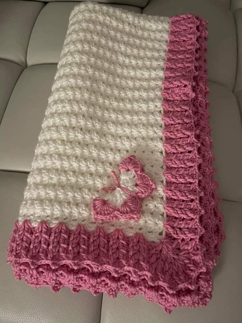 Cream and blush pink handmade crochet baby blanket draped over a cozy chair